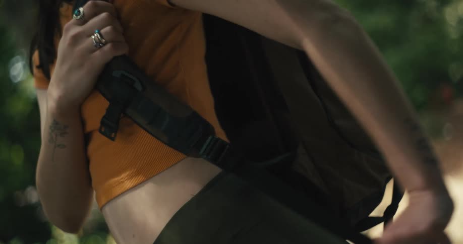 Woman pulls on the strap to tighten the brown backpack she is wearing