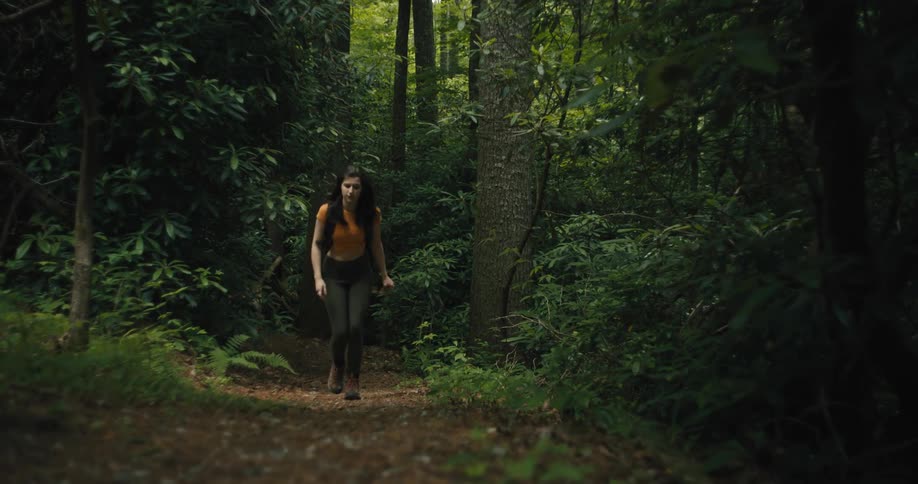 A teenage girl wearing a backpack is walking on a trail through a forest