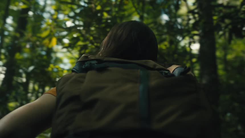 A woman with a brown backpack hiking in the lush green woods