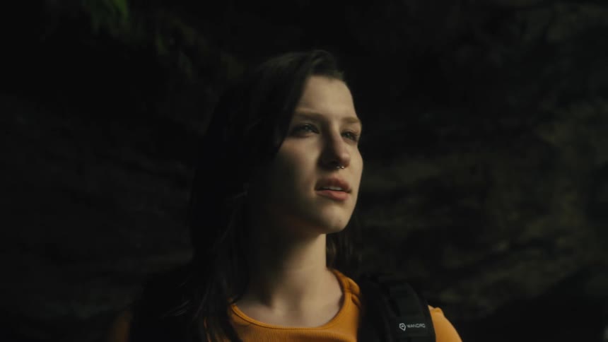 A young woman is walking near rocks and a waterfall