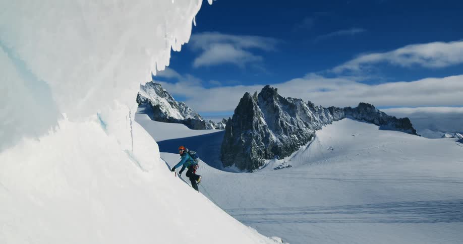 A mountain climber is making his way up a steep snow covered slope