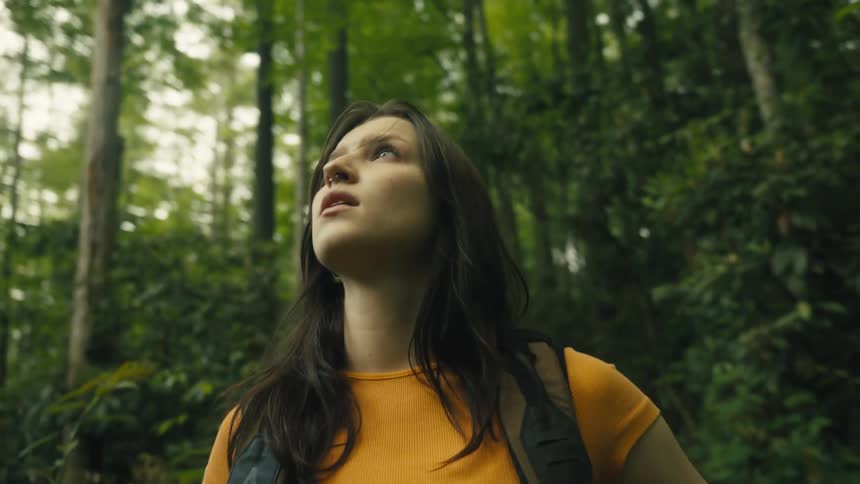Woman wearing an orange t shirt and a backpack walks in the forest