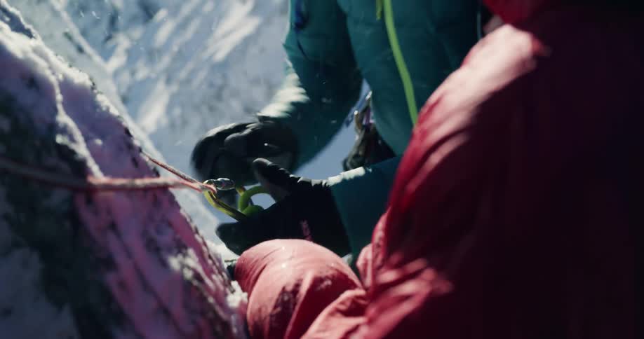 Man and woman adjusting ropes and safety equipment in the midst of a snowy mountain climb