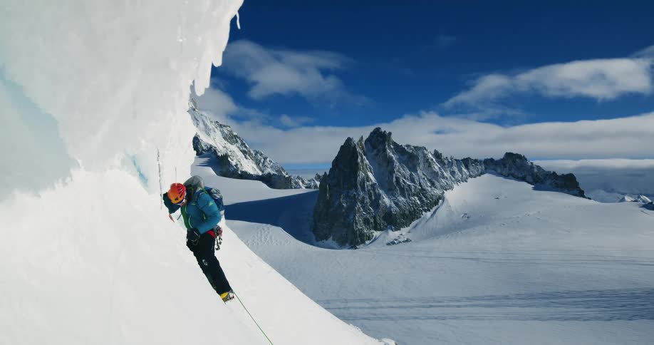 A man climbing a mountain covered in snow at midday
