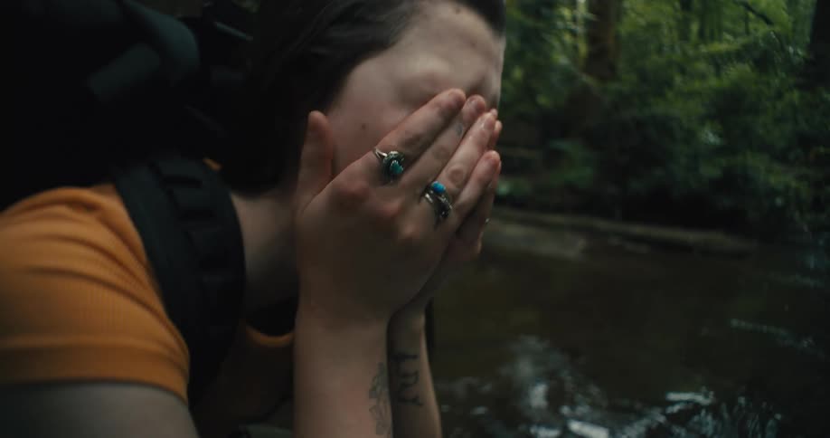A woman wetting her face with river water in the forest