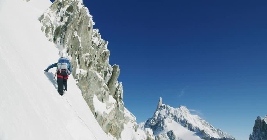 A mountain climber is making his way up a steep snow covered slope