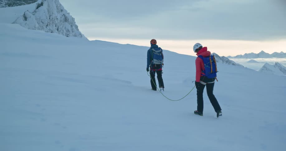 Two people walking in the snowcovered mountains connected by a rope