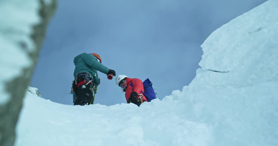 Two mountain climbers drink coffee from a thermos