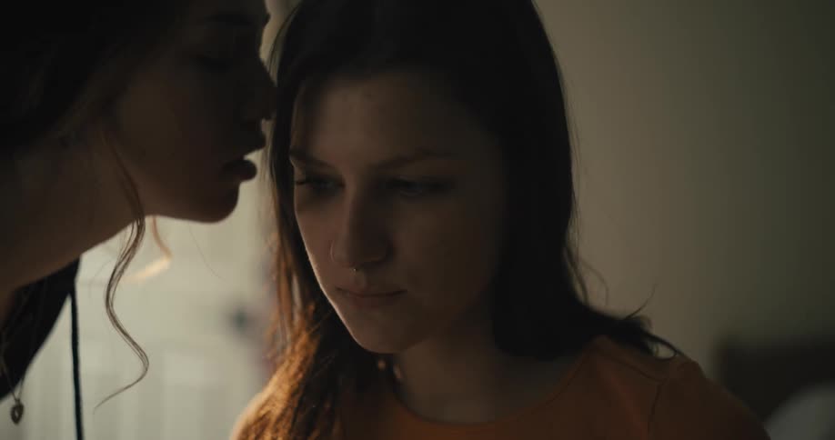 Woman leans over to talk into ear of sitting woman