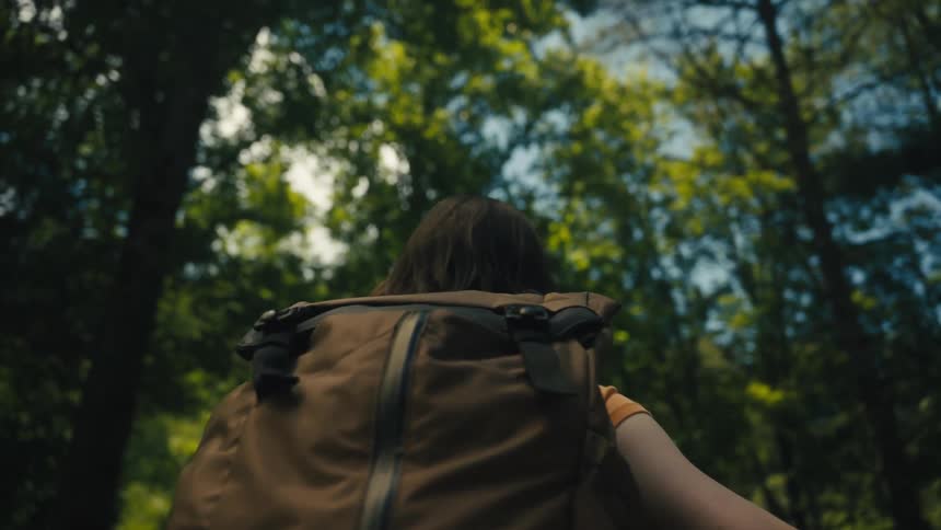 Woman wearing and orange t shirt and a brown backpack walks down in the forest