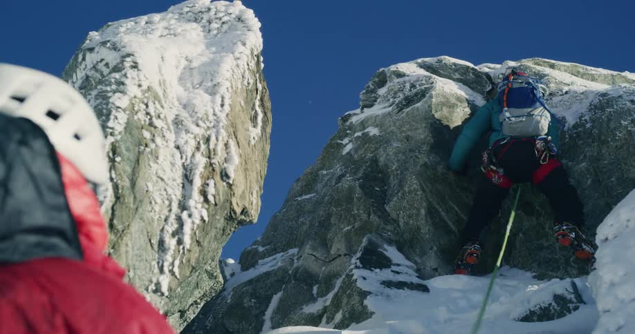 Two mountaineers connected by a safety rope climbing a mountain