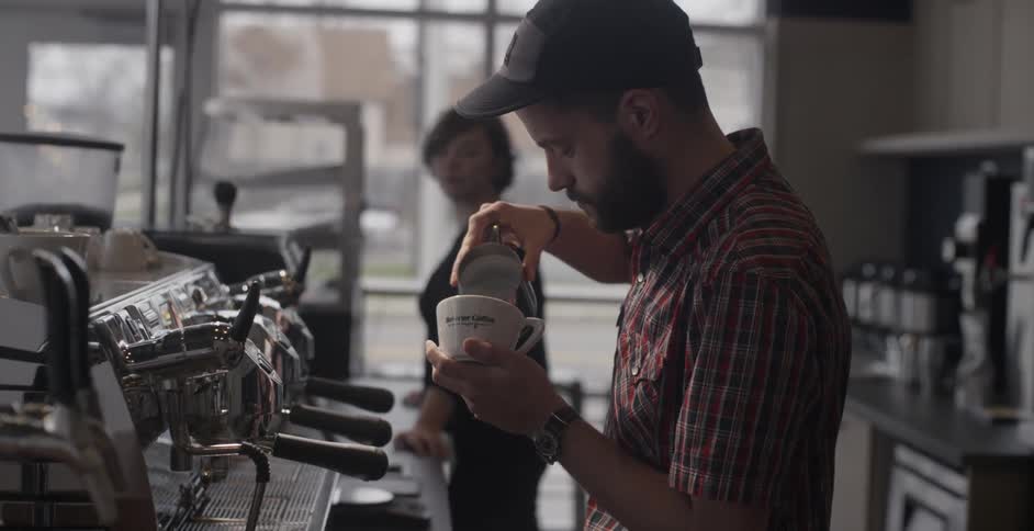 A barista pours creamer into a coffee cup