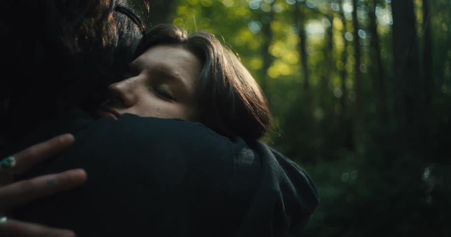 A young girl hugs someone affectionately in an area full of trees