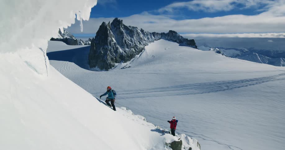 One person climbs up a snowy mountain while the other holds a rope attached to them