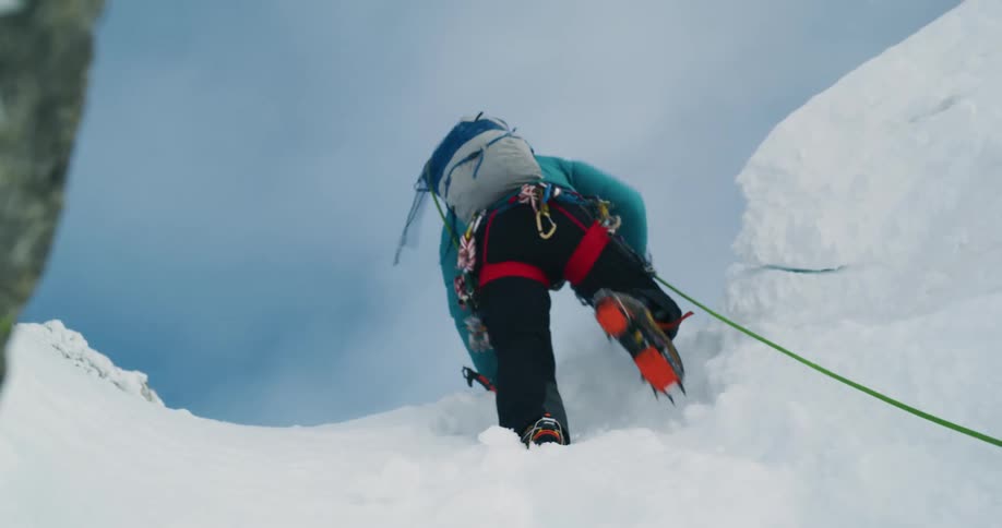 A mountain climber scales a steep slope and reaches the top as his rope hangs behind him