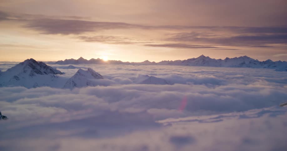 Crest of mountains peaking through the clouds at high altitude during sunset