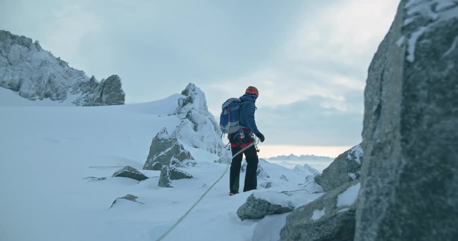 Two mountain climbers walk along the top of a rocky snow covered mountain