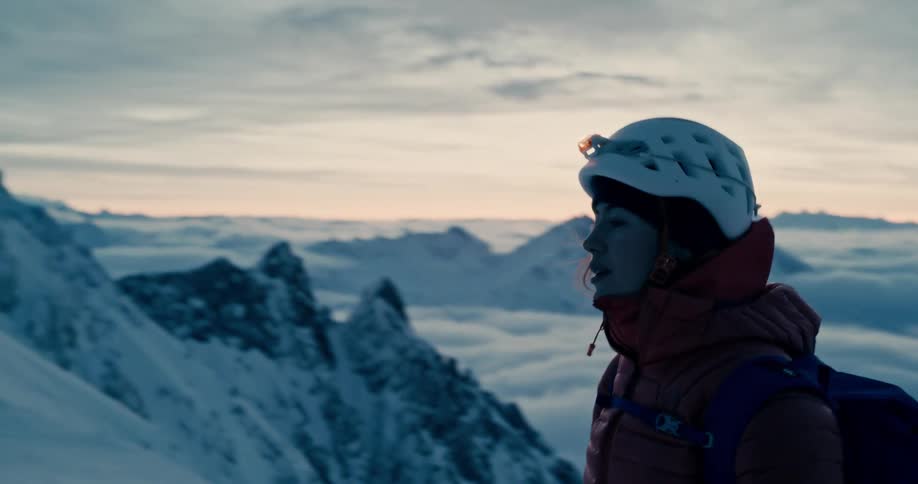 Female hiker walks on a snowy mountain ridge at sunset