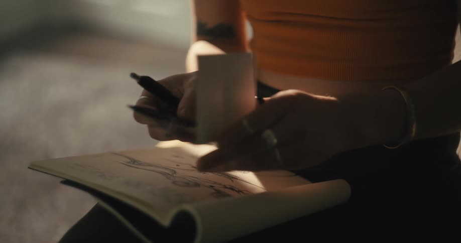 A woman alone in a bedroom contemplates an old photograph as she holds a marker and rests an open magazine on her knees