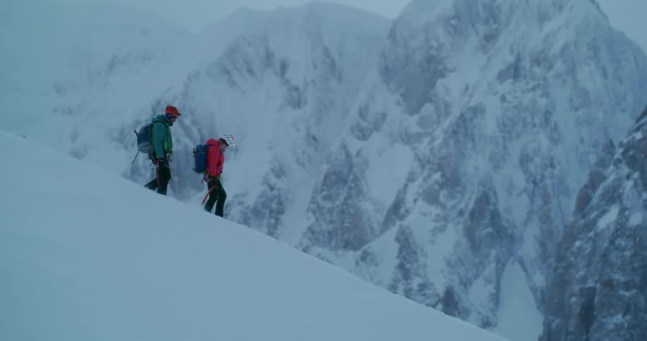 Man and woman walking down a mountain covered in snow at sunset