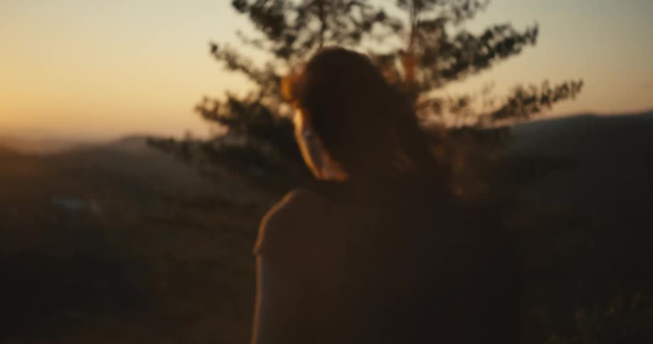 A silhouette of the back of a person who has their hair flying due to the wind and the sun is shining brightly on the spot