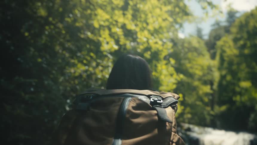Woman wearing a brown backpack hikes in the woods