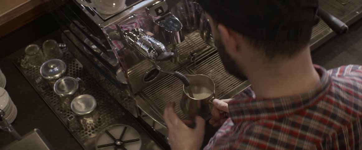 A man uses a coffee machine to fill a metal pitcher