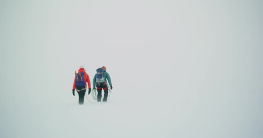 Two mountaineers connected by a safety rope trekking through snow
