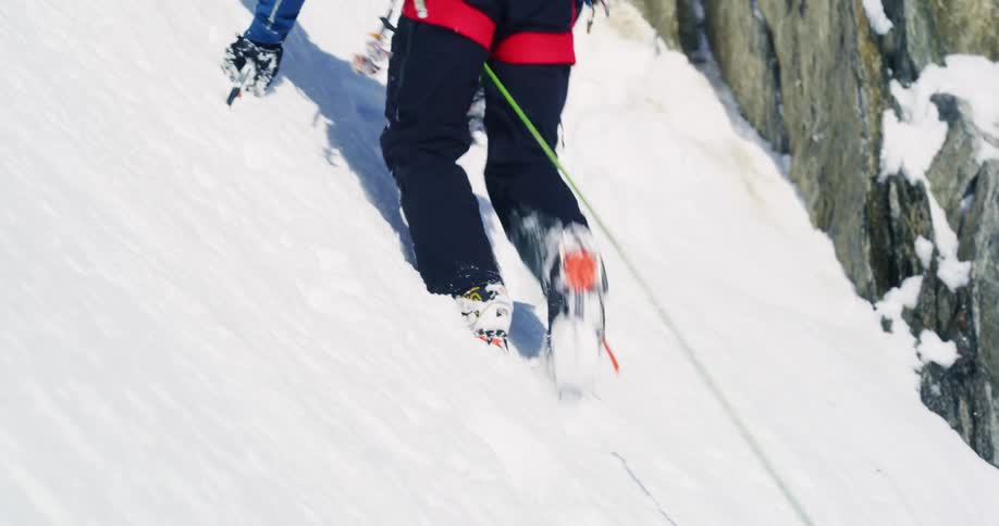 Mountaineer wearing a safety line climbs steep snowy mountain slope