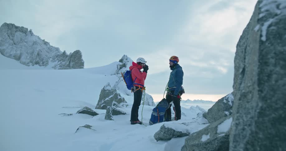 Man and woman in the midst of a snowcovered mountain with one of them holding a drink
