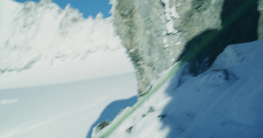 Woman pull on a rope while rock climbing up a snowy mountain during the day