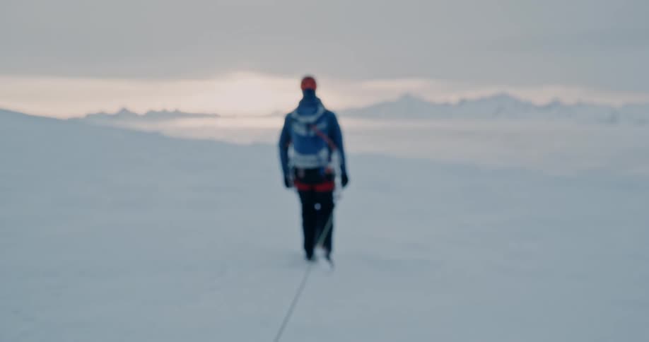 Two people walking connected by a rope on a snowy mountain