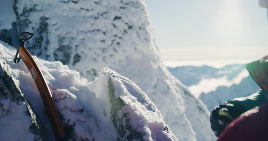 A person removes snow from a rock using a cutting tool and then places a rope on the rock