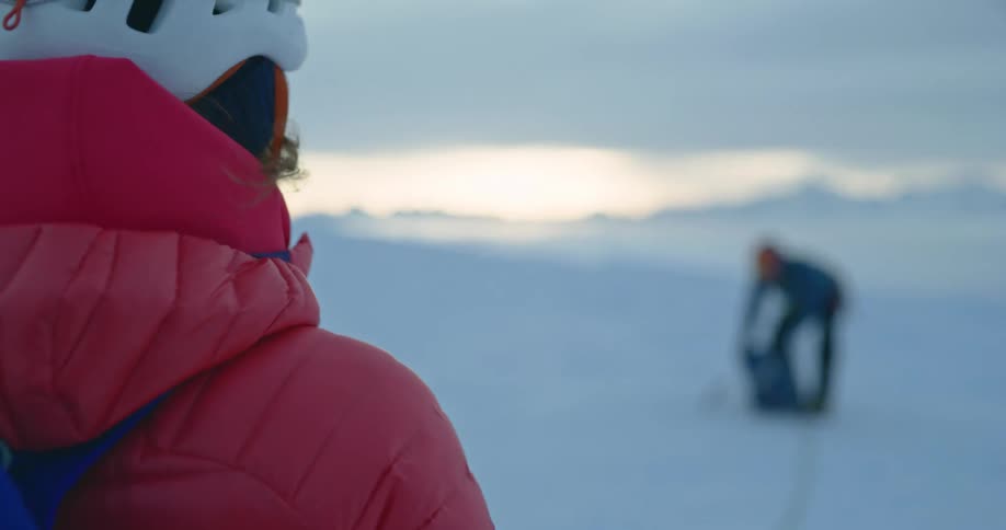 Two people in a snowy area and one of them is putting a rope in his backpack