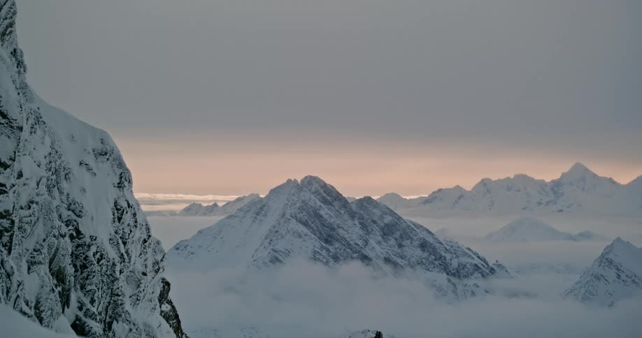 Snowy mountain peaks jut up above a blanket of cloudsat dawn