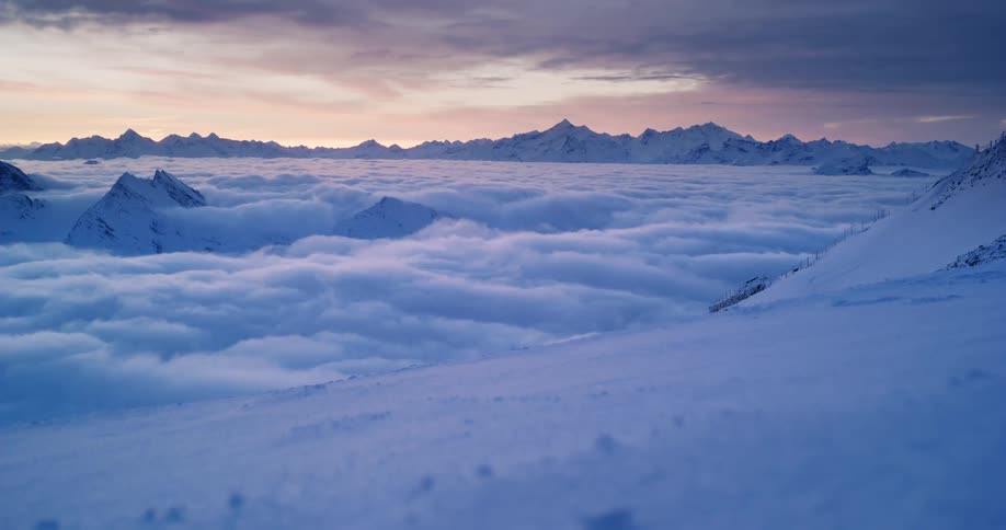 Low lying clouds fill valley between snowy mountain ranges under a red tinted sky
