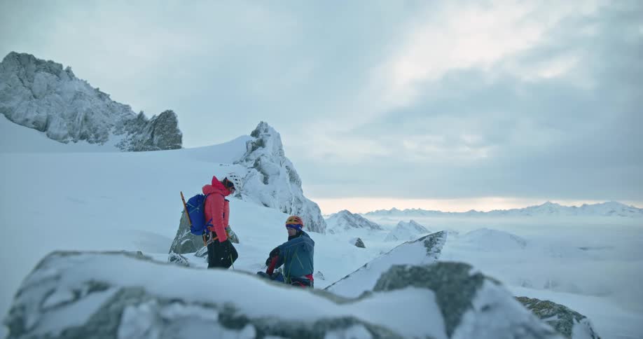 Mountain hikers rest on a snow covered mountain as the sun is setting below the horizon