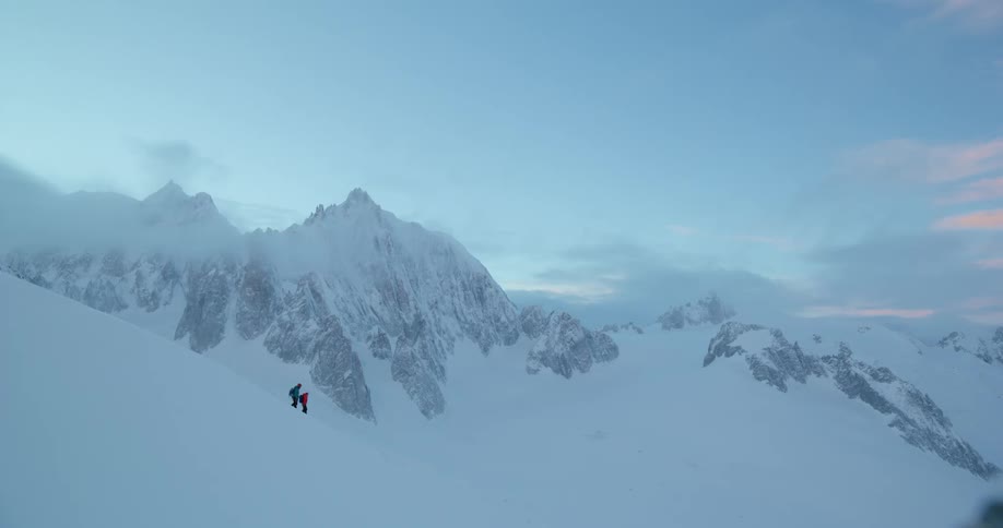 Panorama of a slope with a mountain range and snowcovered peaks and two people trekking