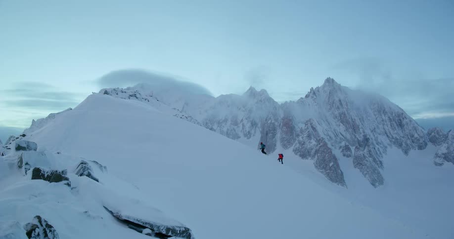 Two people are climbing up the side of a snow covered mountain slope