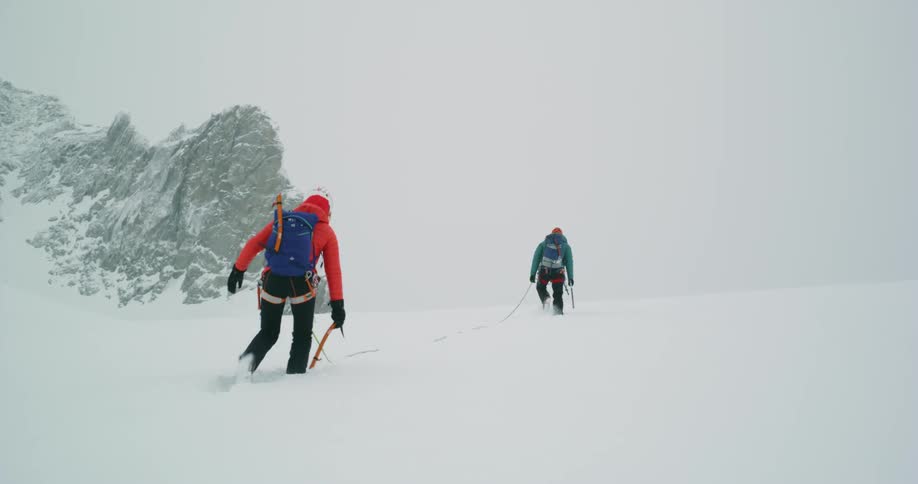 Two people are hiking in the snow during a storm