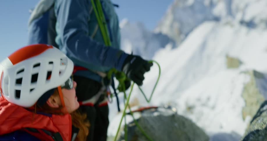 Male climber pulls up rope as female climber climbs snowy mountain slope