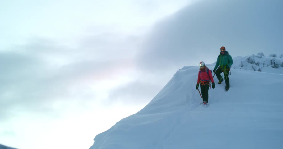 Hikers walk along a snow covered mountain ridge with the sun glowing in the distance