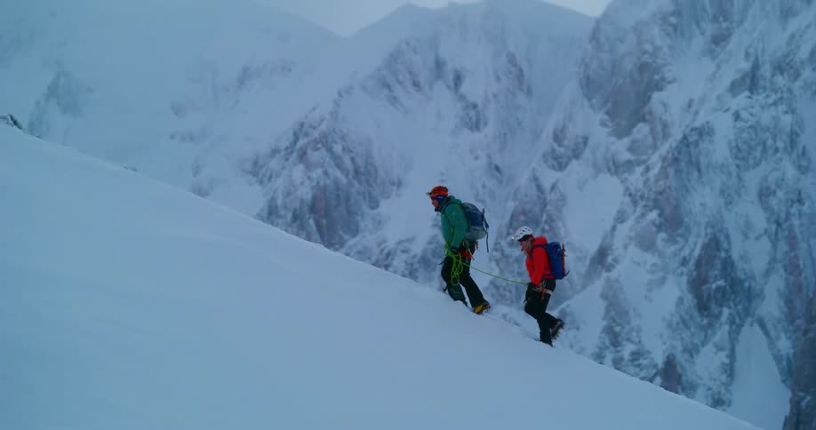 Two people are hiking up the side of a snow covered mountain