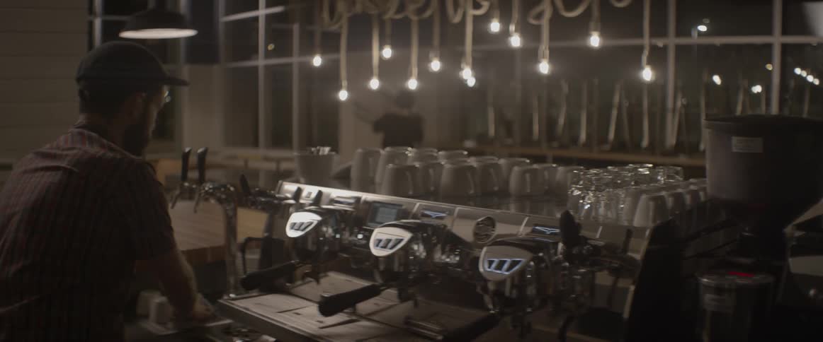 A barista is setting up cups and glasses at his station