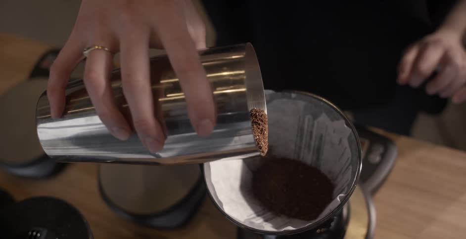 A barista pours coffee grounds into a container