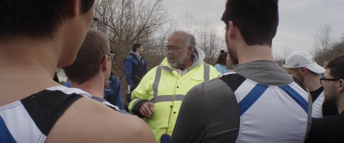 A man in a yellow jacket talks to a group of men on a cloudy day