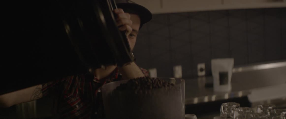 A barista pours coffee beans into a large container