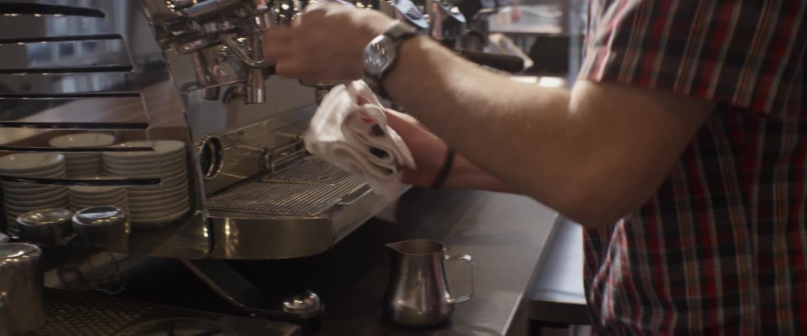 A barista takes a towel and cleans a part on an espresso machine