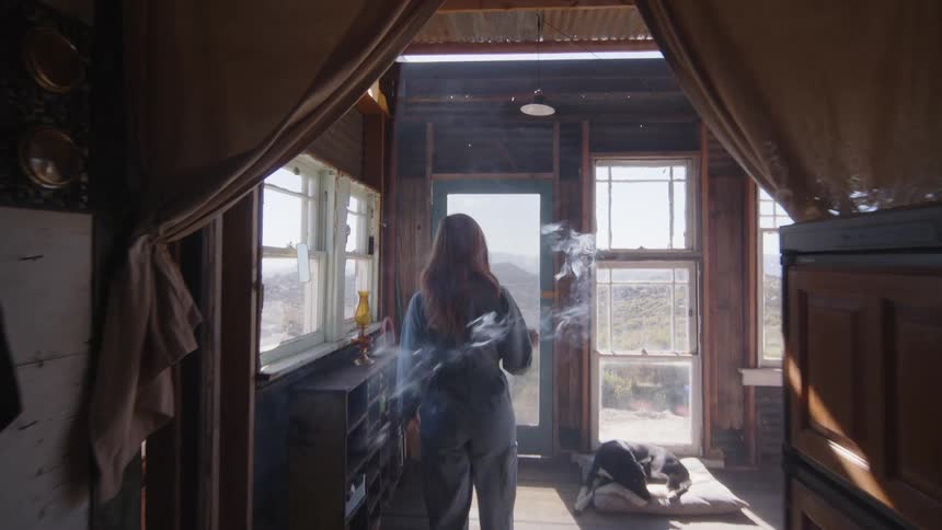 A woman is carrying an incense that is smoking to a table near the window