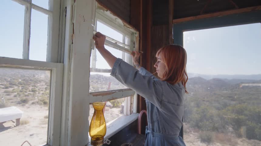 Woman opens the window of a cabin in the countryside